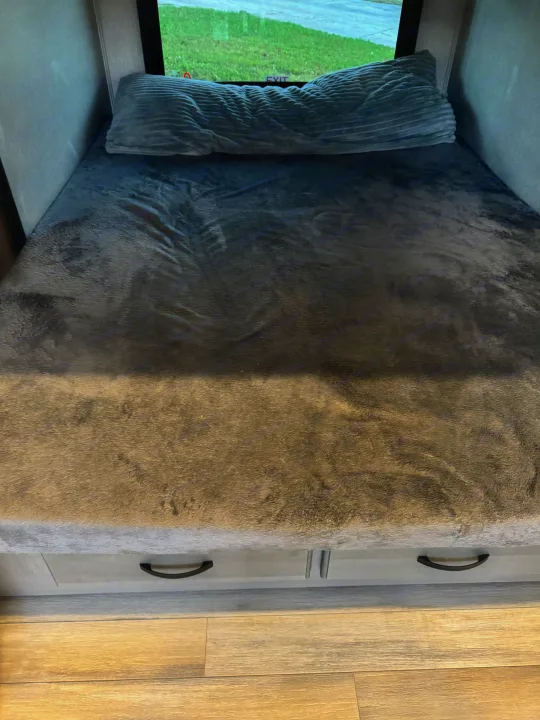 RV rental interior: Comfortable gray bed with ribbed pillow, window view, and practical under-bed storage.. Coachmen Chaparral 2022