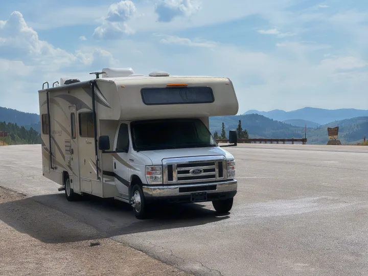 White Class C rv rental motorhome parked on an asphalt pull-off with scenic mountains and cloudy skies at Salt River Pass.. Coachmen Leprechaun 2019