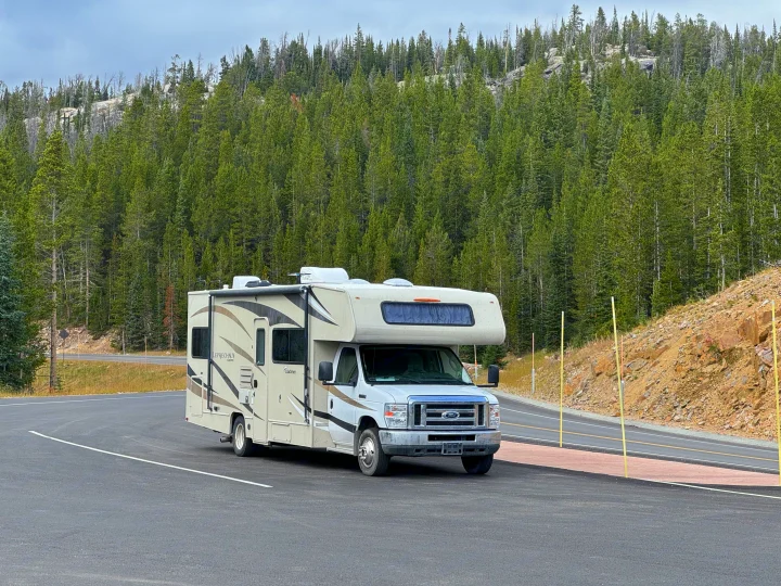 Class C RV rental parked in a scenic forest with dense evergreen trees and rocky hills, perfect for nature travel.. Coachmen Leprechaun 2019