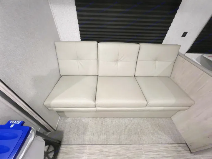 Comfortable light grey bench seating in an RV rental, featuring three cushions, window blinds, and textured walls.. East to West Silver Lake 2022