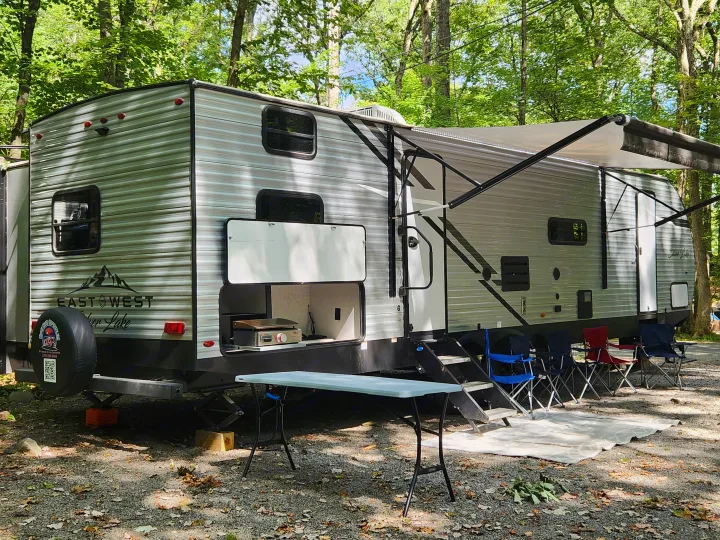 This RV rental at a shady campsite offers an outdoor kitchen, extended awning, and chairs for relaxing.. East to West Silver Lake 2022