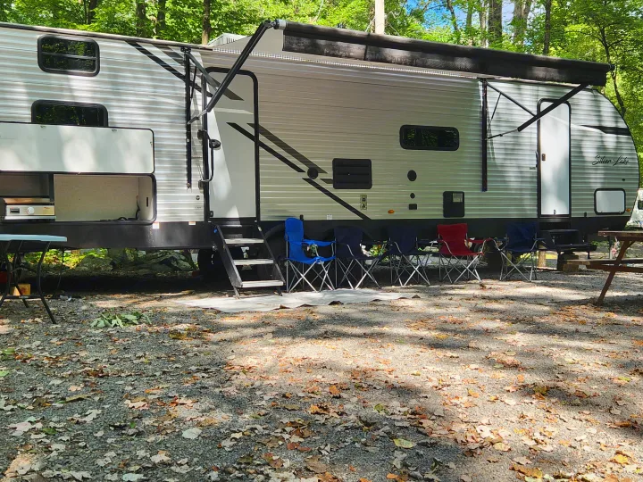 Enjoy a scenic RV rental camping experience with an extended awning, chairs, and picnic table at a shaded, leafy site.. East to West Silver Lake 2022