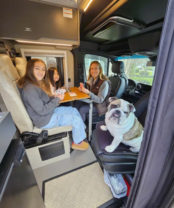 Inside a spacious RV rental, a family of three and their bulldog play cards, enjoying quality time.. Entegra Coach Launch 2023