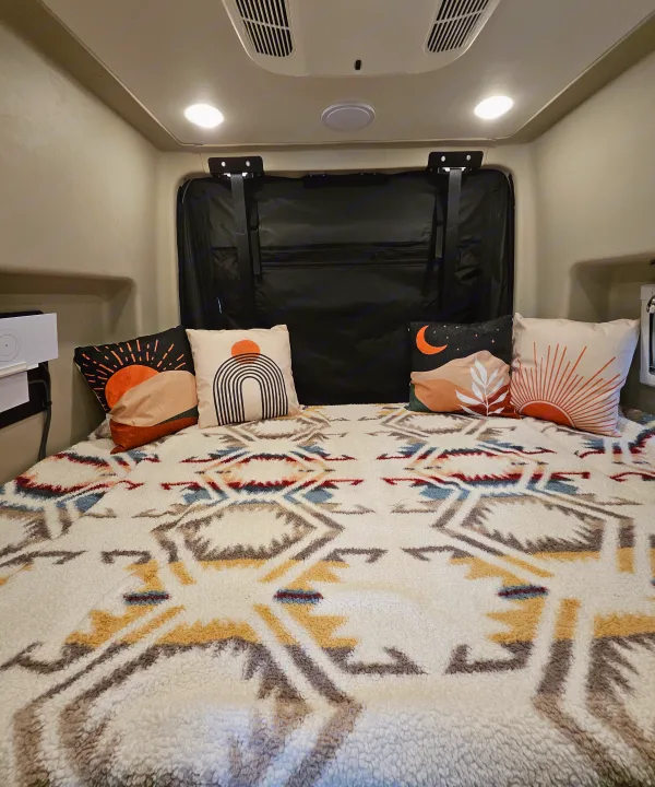 Comfortable RV rental bed with stylish desert-themed pillows & a warm, textured geometric blanket for cozy travels.. Entegra Coach Launch 2023