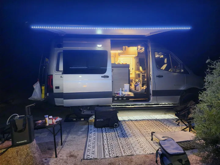 Cozy night in an RV rental with bright awning lights, an outdoor rug, and a happy bulldog enjoying van life.. Entegra Coach Launch 2023
