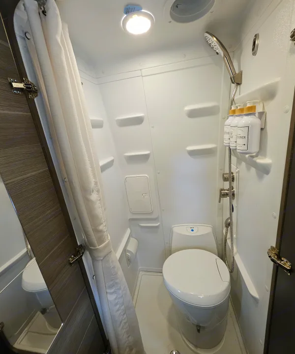 An RV rental's bright, compact bathroom showing a toilet, shower, and organized shampoo bottles.. Entegra Coach Launch 2023