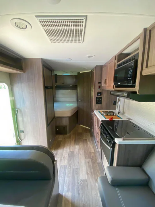 This clean RV rental interior offers a full kitchen, a comfortable bed, and a living area with wood-look flooring.. Winnebago Minnie Winnie 2020