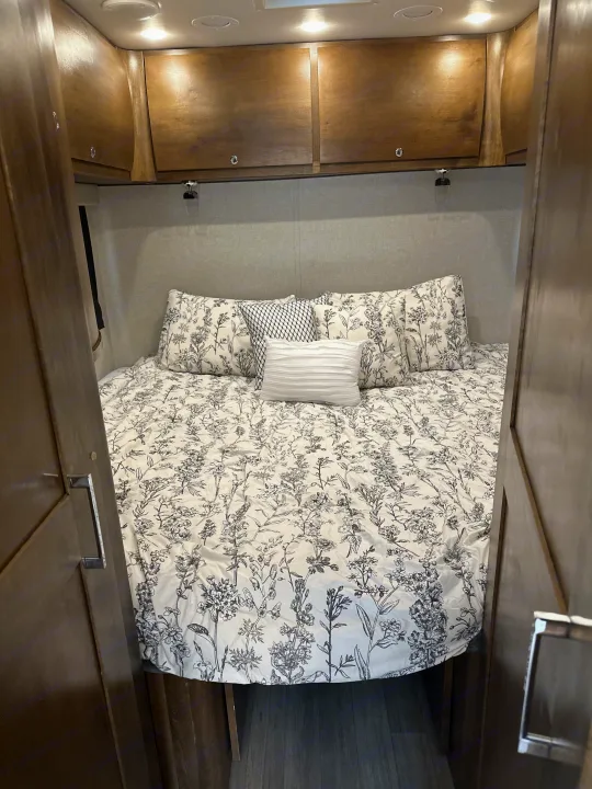 Step into this comfortable rv rental bedroom, featuring floral bedding, spacious overhead cabinets, and soft lighting.. Wayfarer Wayfarer Motorhome 2018