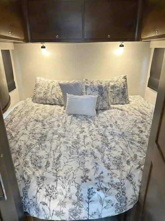 This comfortable RV rental bedroom features a large bed with black and white floral bedding, decorative pillows, and reading lights.. Wayfarer Wayfarer Motorhome 2018