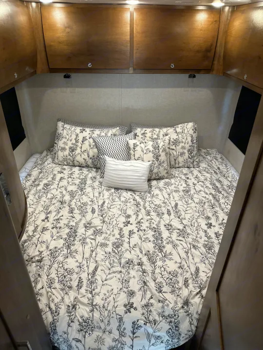 Cozy RV rental bedroom featuring floral bedding, plush pillows, and wooden overhead cabinets.. Wayfarer Wayfarer Motorhome 2018