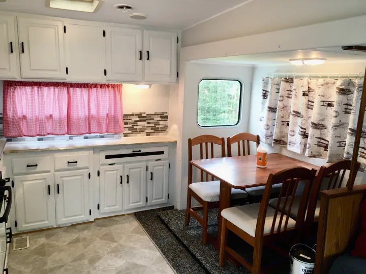 Bright RV rental interior: white kitchen cabinets with red gingham curtains, and a dining area with wooden table and chairs.. Jayco Eagle 1998