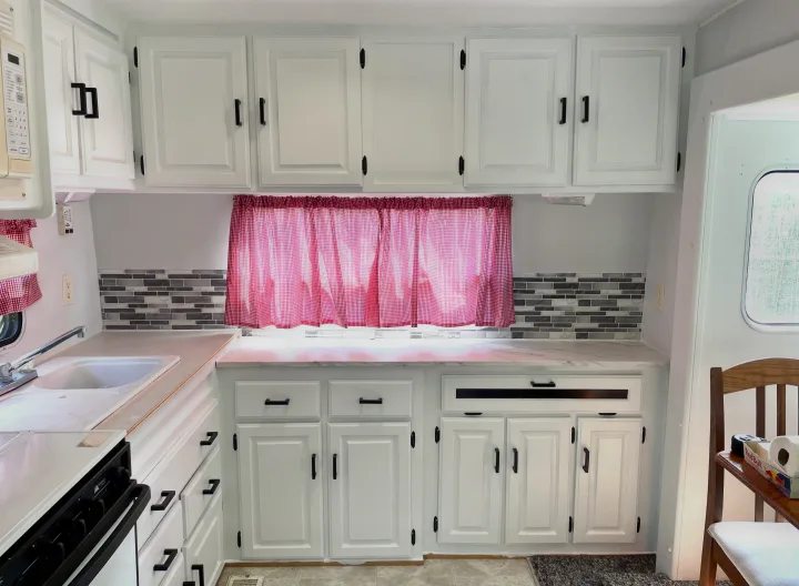 Bright RV rental kitchen featuring updated white cabinets, black hardware, new tile backsplash, and cheerful red curtains.. Jayco Eagle 1998