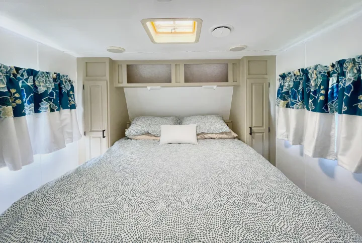 Enjoy a cozy RV rental bedroom. Features include patterned bedding, blue floral valance curtains, and ample overhead storage.. Jayco Eagle 1998
