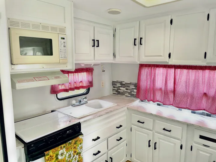 Clean, updated RV rental kitchen with white cabinets, marble-look counters, and charming red gingham curtains.. Jayco Eagle 1998