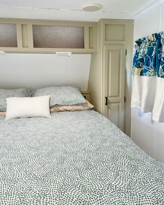 Cozy RV rental bedroom featuring patterned bedding, overhead cabinets, and bright floral curtains for a comfy stay.. Jayco Eagle 1998