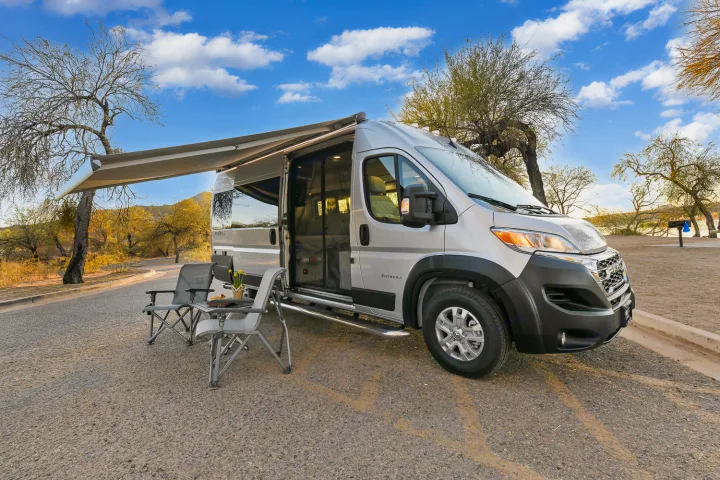 Silver camper van RV rental with awning extended and chairs set for outdoor leisure.. Entegra Coach Ethos 2024
