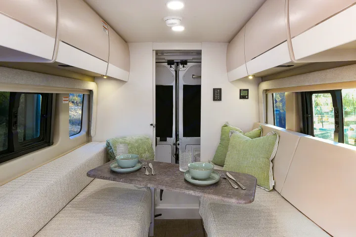Spacious rv rental living area: A bright interior with opposite benches, a central table, overhead cabinets, and large windows.. Entegra Coach Ethos 2024