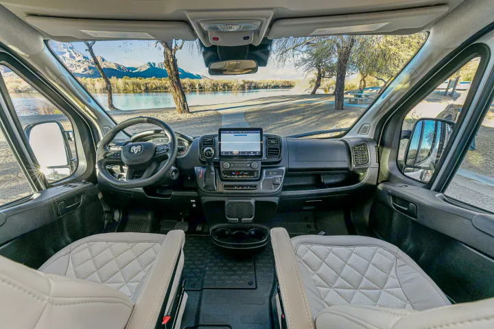 RV rental's modern cockpit, featuring a large touchscreen, steering wheel, and a scenic lake-mountain vista outside.. Entegra Coach Ethos 2024