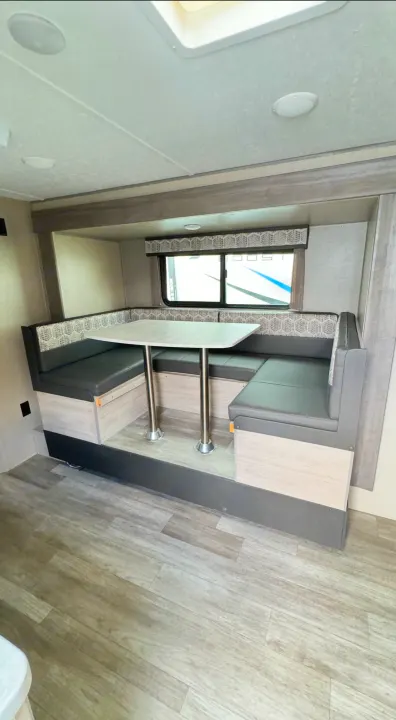 Modern rv rental dinette with U-shaped booth seating, dark cushions, patterned backrests, and a light table.. Coachmen Catalina 2023