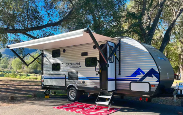 Scenic **rv rental**: A Catalina Summit Series travel trailer with its awning extended, parked at a peaceful campground.. Coachmen Catalina 2023
