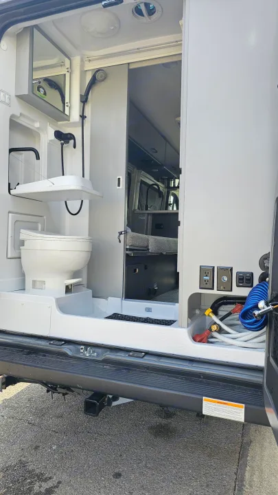 View the compact bathroom, featuring a toilet and shower, and utility panel of this RV rental, ready for your next adventure.. Thor Motor Coach Dazzle 2025