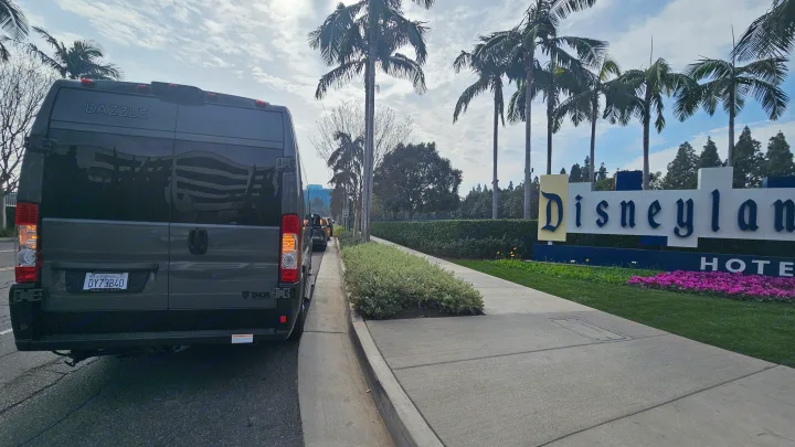 An RV rental van, labeled 'DAZZLE', parked beside the iconic Disneyland Hotel sign amidst palm trees.. Thor Motor Coach Dazzle 2025