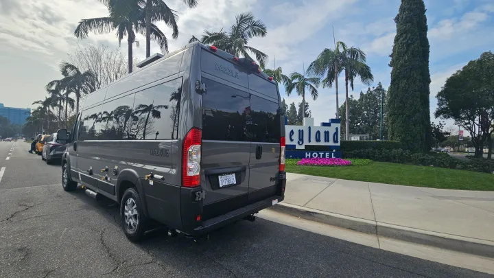 A dark grey Dazzle RV rental parked by the Disneyland Hotel sign. Palm trees reflect in its dark windows.. Thor Motor Coach Dazzle 2025