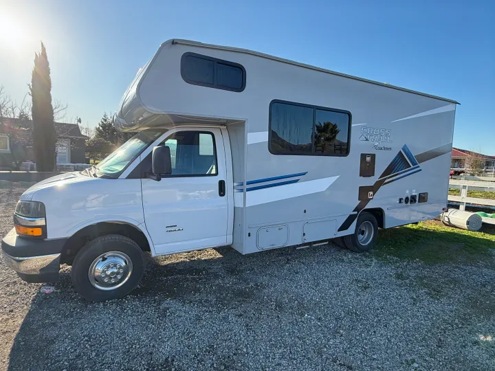 Class C RV rental: A light gray Coachmen Cross Trail, parked on gravel under bright sun.. 1HAGGUC78MN008793 Cross Trail 2022