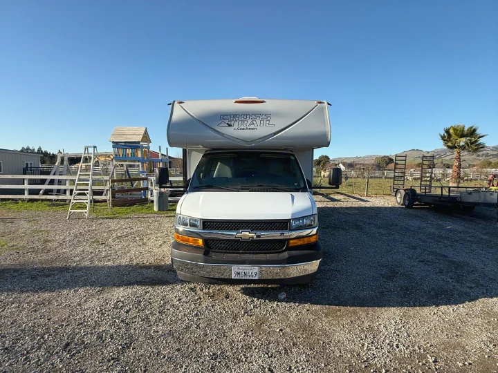 White Coachmen Cross Trail RV rental parked on gravel, with a playset and hills in the background under a clear blue sky.. 1HAGGUC78MN008793 Cross Trail 2022