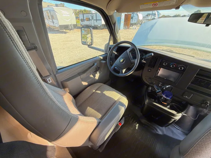 View inside an RV rental van's driver cabin, showing the dashboard, steering wheel, and parked RVs outside.. 1HAGGUC78MN008793 Cross Trail 2022