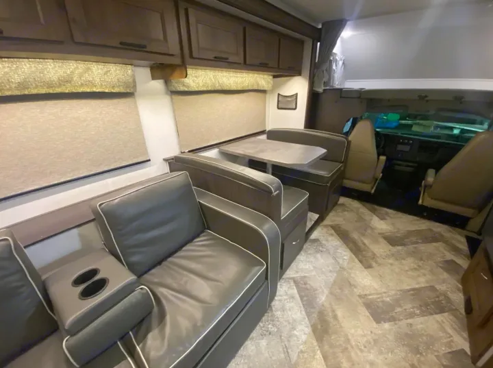 Spacious rv rental interior showing a sofa, dinette with table, overhead cabinets, and cockpit view. Ideal for travel.. Forest River Forester 2020