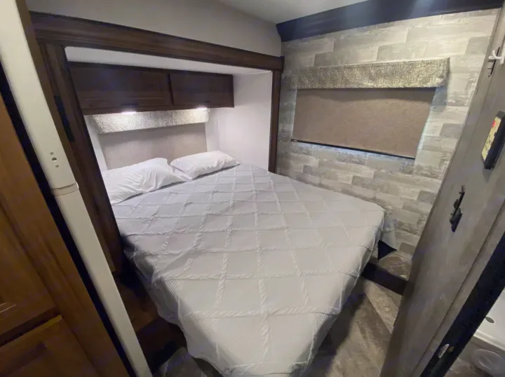 Cozy RV rental bedroom with a comfortable bed, overhead storage, and textured wall, ideal for travel.. Forest River Forester 2020