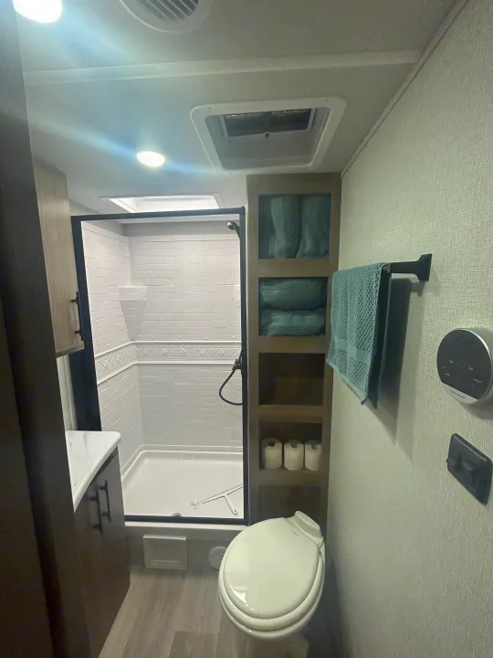 RV rental: Modern compact bathroom with white shower, toilet, shelving, and vanity for convenient travel.. Grand Design Imagine XLS 2024
