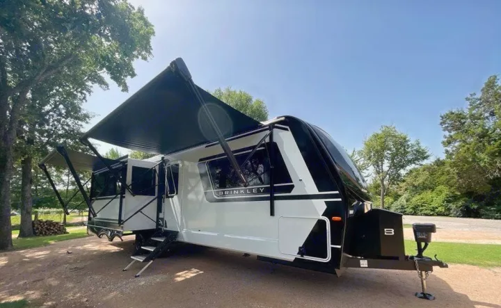 Modern Brinkley RV rental travel trailer with black & white design & extended awning at a shaded campsite.. Brinkley 295 AIR 2025