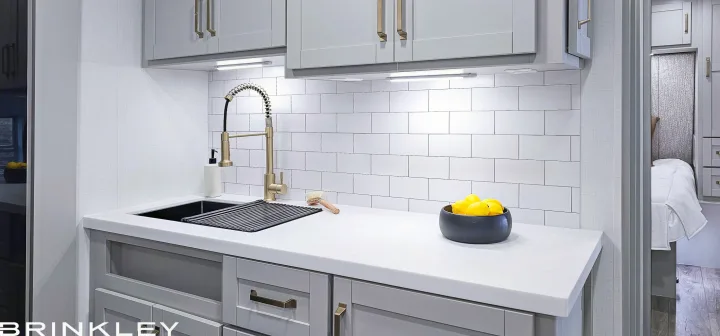 Stylish RV rental galley with grey cabinets, white countertop, subway tile, and a gold faucet. Ideal for compact living.. Brinkley 295 AIR 2025