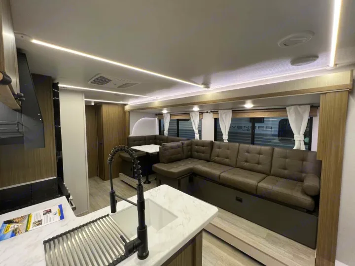 Inside a modern rv rental: kitchen with sink, comfy U-shaped sofa, and dining table. Bright interior.. Forest River Wildwood X-Lite 2025