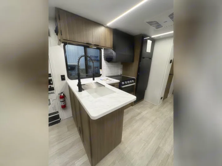 Modern RV rental kitchen showcasing a sink island, black appliances, wood cabinets, and light flooring.. Forest River Wildwood X-Lite 2025