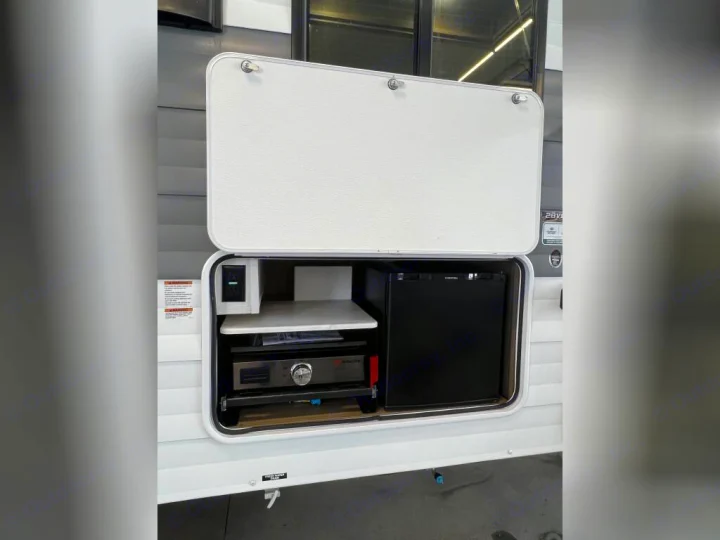 RV rental outdoor kitchen setup: a griddle, mini-fridge, and power outlet inside an open compartment.. Forest River Wildwood X-Lite 2025
