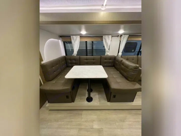 Spacious RV rental interior: U-shaped lounge seating with a white table and ample windows, ideal for relaxing & dining.. Forest River Wildwood X-Lite 2025