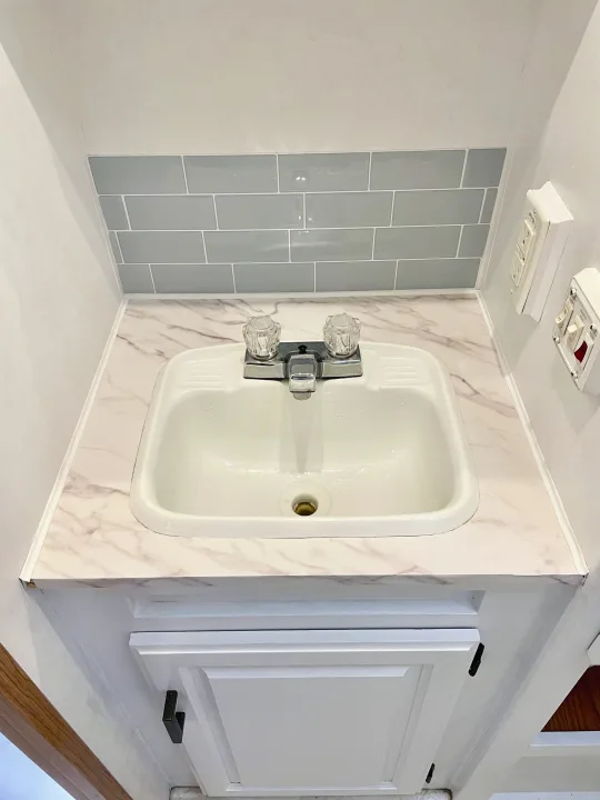 Clean RV rental bathroom featuring a white sink, marble-look countertop, gray subway tile backsplash, and RV utility controls.. Jayco Eagle 1998