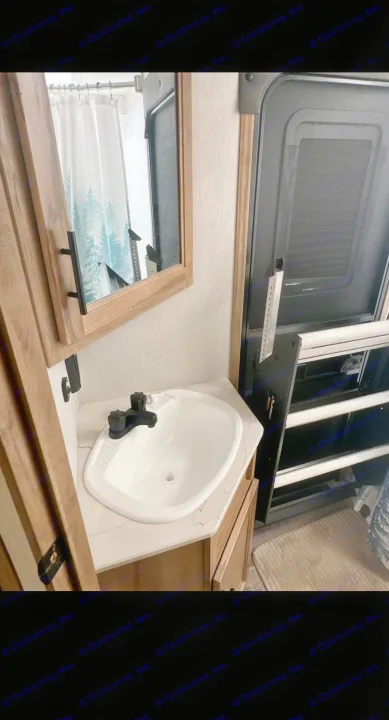RV rental: A cozy bathroom area featuring a white sink, wood vanity, and mirror. The shower curtain is reflected. Ladder by door.. Forest River Cherokee Alpha Wolf 2023