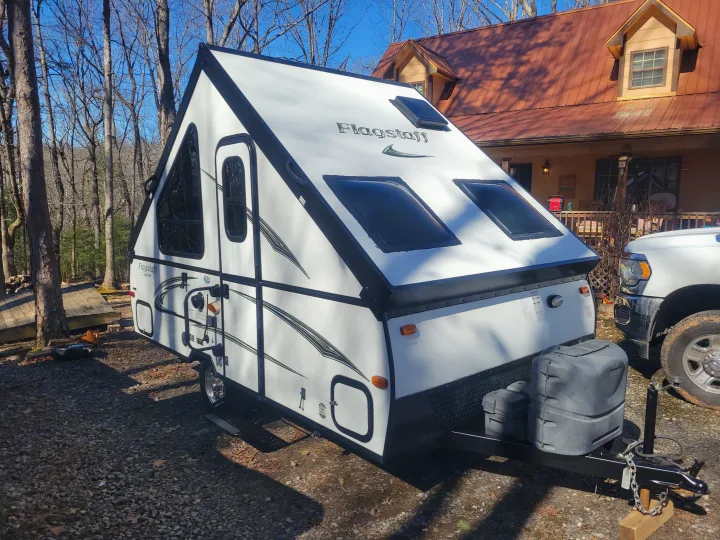 This white Flagstaff A-frame camper, ideal for an RV rental, is parked outdoors near a house and trees.. Flagstaff A Frame 2015