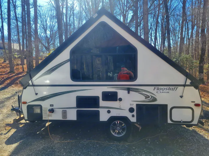 White Flagstaff Classic A-frame RV rental parked on gravel, surrounded by bare trees. Perfect for adventure!. Flagstaff A Frame 2015