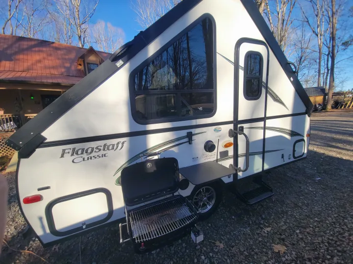 Enjoy an A-frame Flagstaff RV rental setup with a side-mounted grill and table, ideal for outdoor cooking and camping.. Flagstaff A Frame 2015