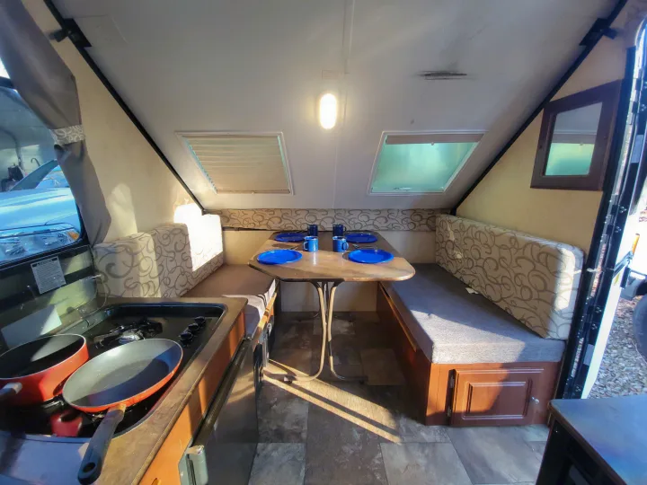 Inside an rv rental pop-up camper, showing a dining area with table and benches, plus a small kitchen stove.. Flagstaff A Frame 2015