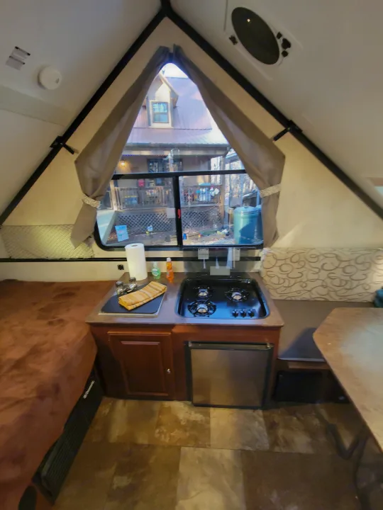 RV rental interior showing a compact kitchen with stove/sink, bed, dining area, and exterior view through the window.. Flagstaff A Frame 2015