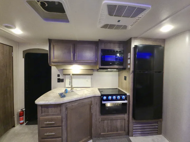 Explore this cozy RV rental kitchen: sink, stove, microwave, fridge, and ample storage, ideal for road trips.. Forest River Aurora Aurora 2021