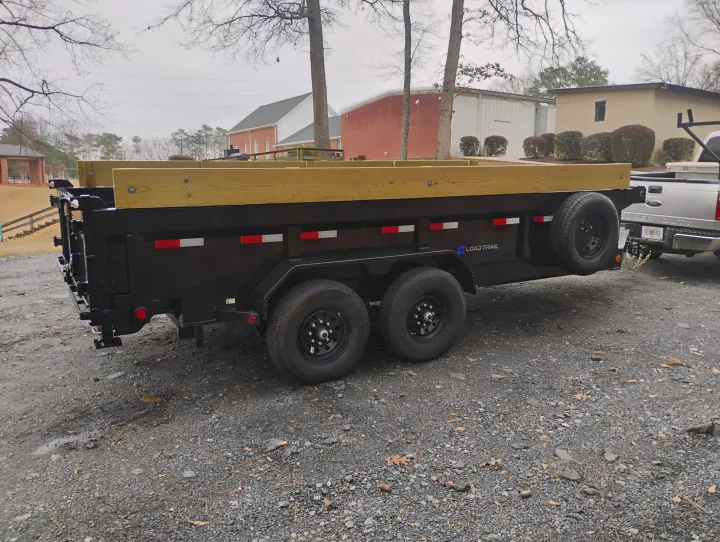 Black Load Trail dump trailer with wooden sides hitched to a Ford Super Duty truck, great for rv rental hauling.. Load Trail Dump Trailer 2025