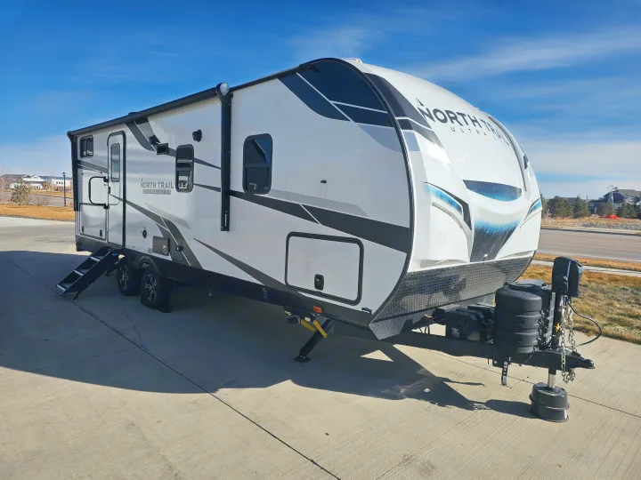 White travel trailer with black/grey graphics, ideal for an RV rental, parked on concrete on a sunny day.. Heartland RVs North Trail 2024
