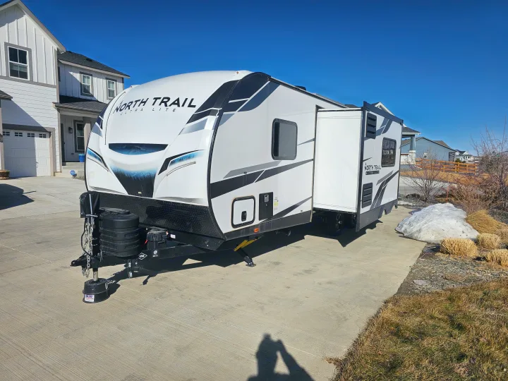 This North Trail Ultra Lite travel trailer with slide-out is parked on a driveway, ready for RV rental adventures.. Heartland RVs North Trail 2024